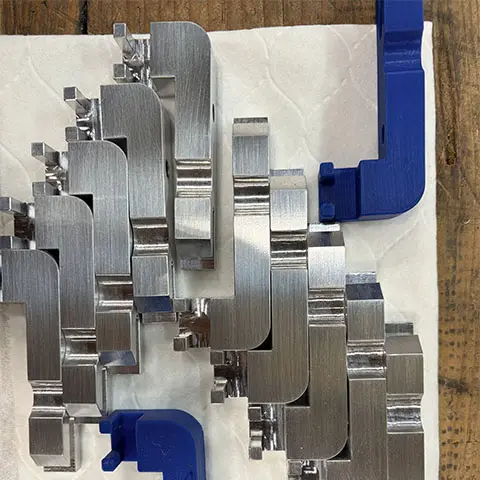 Precision machined aluminum brackets next to a 3D-printed sample part, showing Astro Tool & Machine Co.'s reverse engineering process.