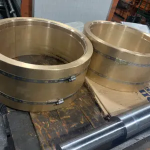 Large Custom Bronze Bearing Shells — Astro Tool & Machine Co. Two large custom bronze bearing shells next to a precision machined shaft at Astro Tool & Machine Co.